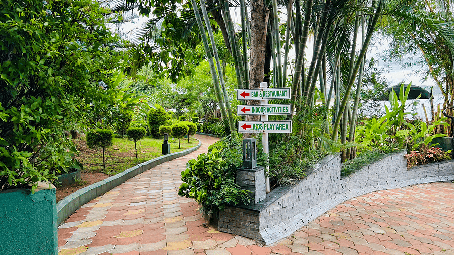 Image of a pathway with a signboard in the middle and plants around it at Coorg Jungle Camp.