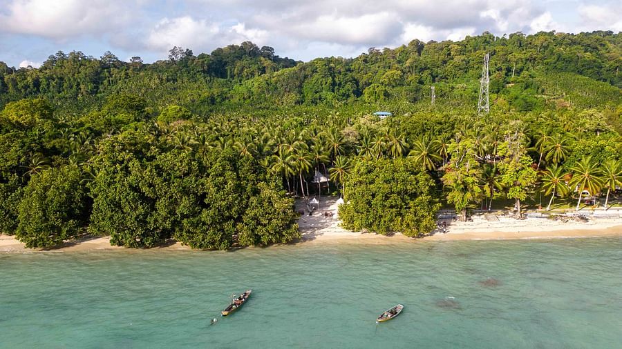 A close-up aerial view of a beach area, showing kayaks and lounge chairs along the shoreline. The crystal-clear water and surrounding tropical trees create a relaxing atmosphere - Coral Reef Resort & Spa, Havelock