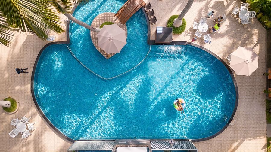 An aerial view of a beautifully designed pool shaped like a heart, surrounded by lush greenery and palm trees. The water is crystal clear, creating a serene setting - Coral Reef Resort & Spa, Havelock