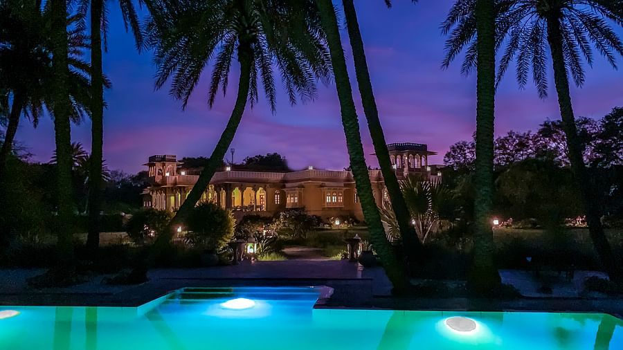 image of the swimming pool at Dev Shree, Deogarh overlooking a beautiful sky post sunset and tall palm trees