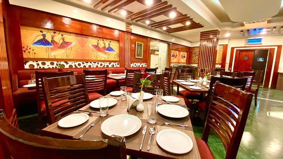 Dining area at DLS Park Grace, Haridwar featuring wooden chairs, ceramic plates, wall art and false ceiling.