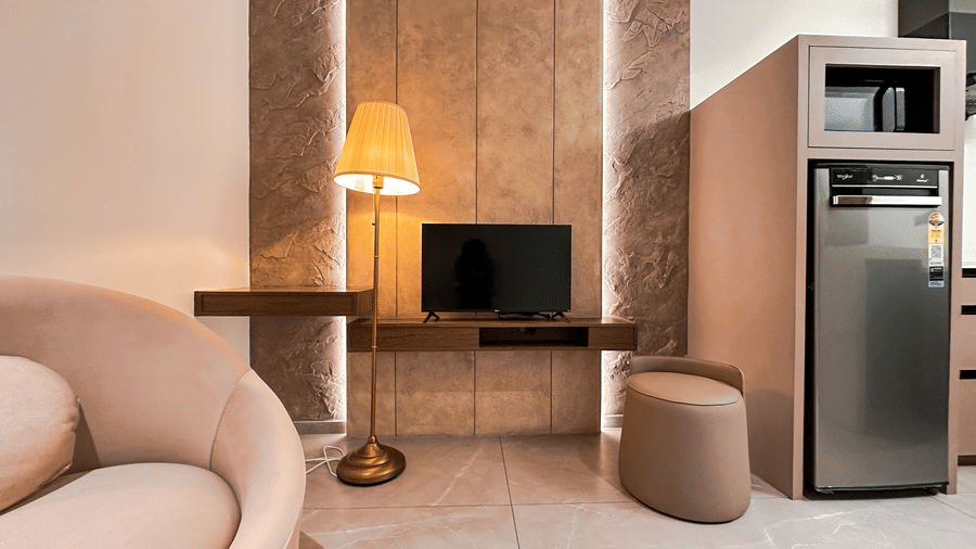 A television kept on a wooden float alongside a tall brightly lit lamp in the Apartment Suite at F Hotels, Bengaluru.