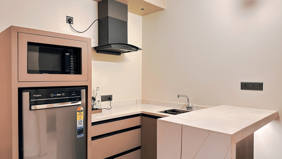 A close up of the kitchenette coutertop, featuring a modular chimney, microwave, and a refridgerator at F Hotels, Bengaluru.
