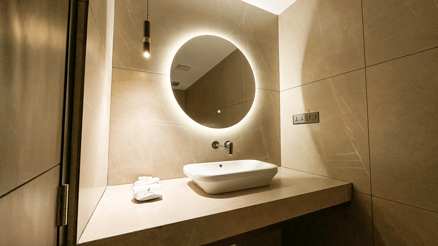 A wash basin along with a backlit round mirror in the bathroom of the Deluxe Room at F Hotels, Bengaluru.