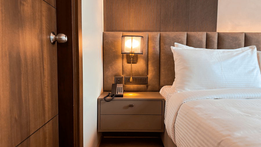 A close-up shot of the bed side table beside a plush bedding with a tufted headboard in the Executive Room at F Hotels, Bengaluru.