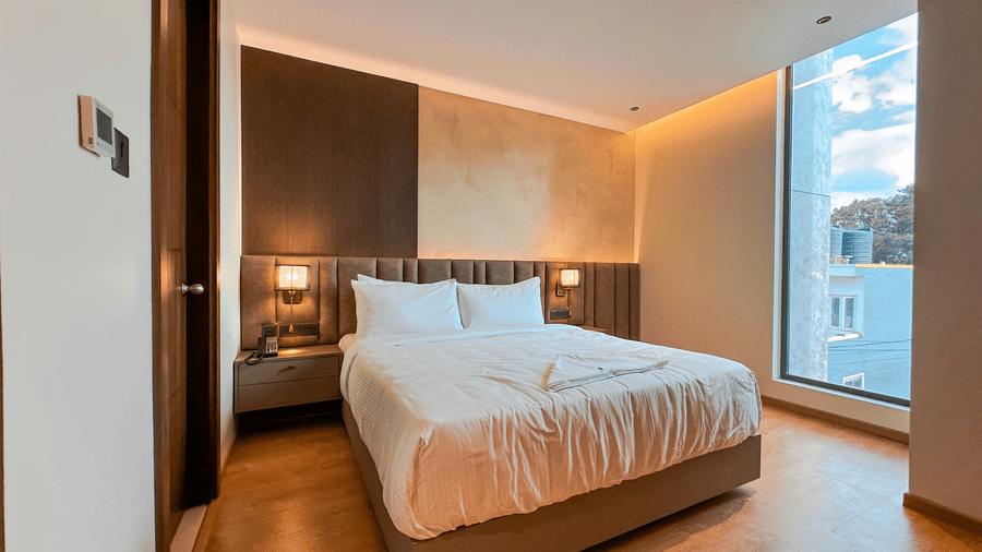 A wide-angle shot of the Executive Room featuring a plush double bed with bed side tables on either side of the bed at F Hotels, Bengaluru.