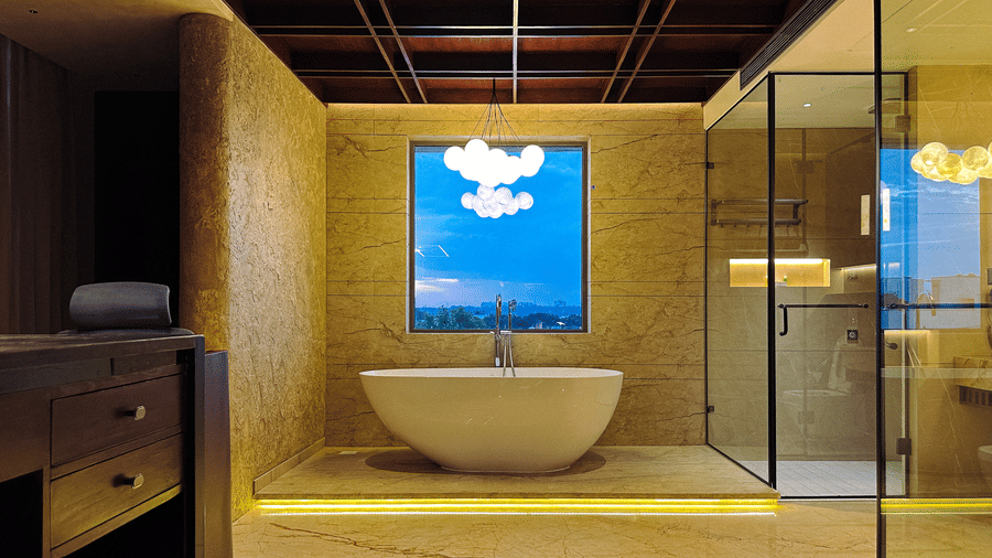 Front view of the wash basin with a square window overlooking the evening skies of the city from the bathroom of the Honeymoon Suite at F Hotels, Bengaluru.