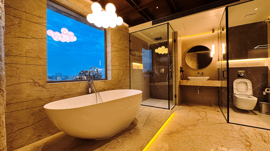 Full view of the bathroom featuring a bathtub, a shower cubical, a commode separated by glass doors in the bright lit bathroom of the Honeymoon Suite of F Hotels, Bengaluru.