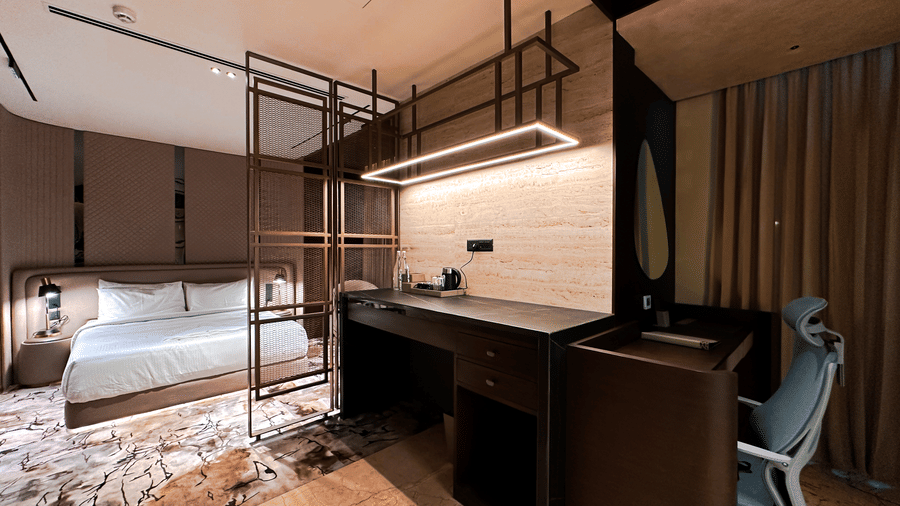 A wide-angle shot of the Honeymoon Suite featuring a work station under a modern light fixture above it, overlooking the double bed at F Hotels, Bengaluru.