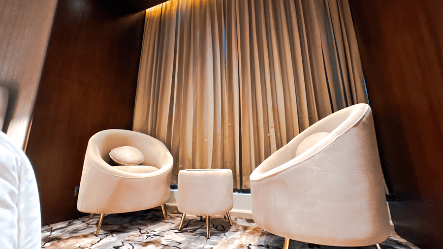 Close-up shot of the common seating area with 2 armchairs along with a small coffee table in between at the bedroom of the Honeymoon Suite at F Hotels, Bengaluru.