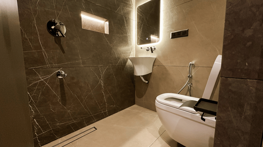 The common bathroom for the pods featuring a tiny wash basin along with a backlit mirror, a commode, and a shower head at F Hotels, Bengaluru.