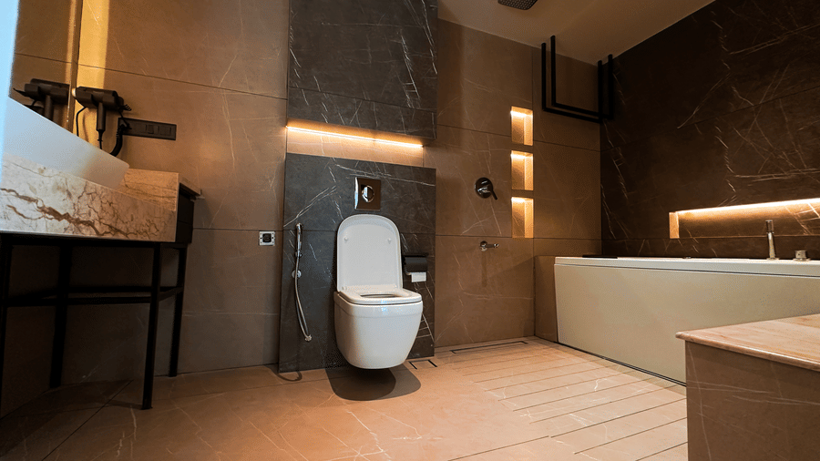 A wide-angle shot of the bathroom of the Presidential Suite featuring a commode, a bathtub, and vanity area at F Hotels, Bengaluru.