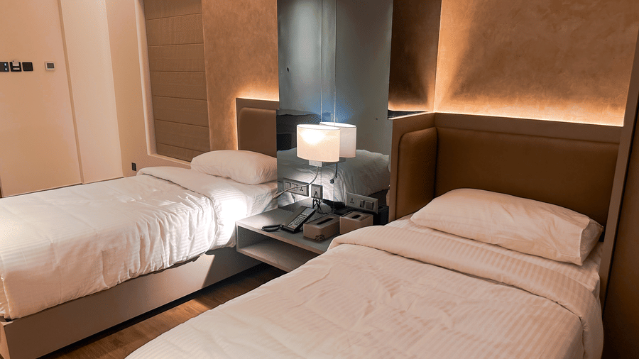 Close up of the twin bed setup at the Superior Room with a brightly lit table lamp on the bed side table between the 2 beds at F Hotels, Bengaluru.