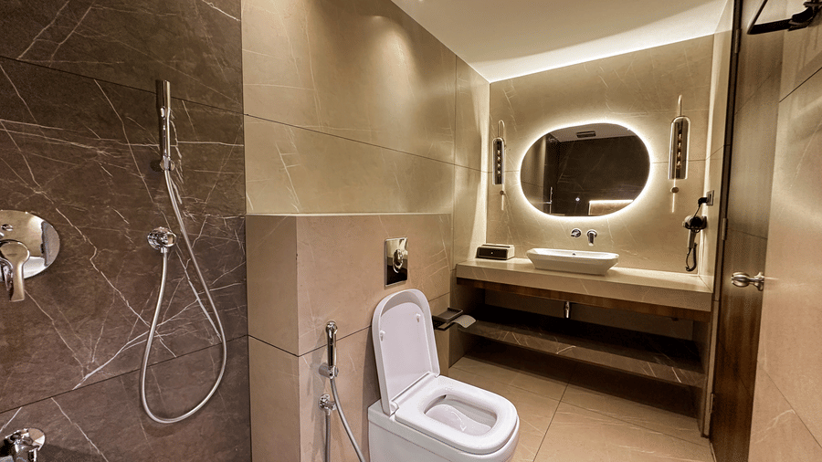 A brightly lit bathroom at the Superior Room featuring a backlit mirror above the wash basin at F Hotels, Bengaluru.