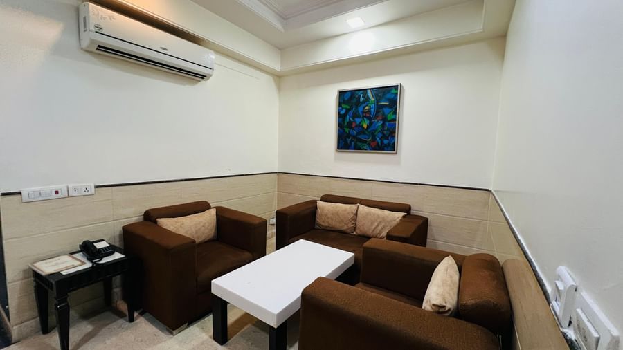 A bright hotel suite with a golden sofa set, a coffee table, and a framed artwork, exuding a warm and inviting feel. | Suite | Hotel Aadhar