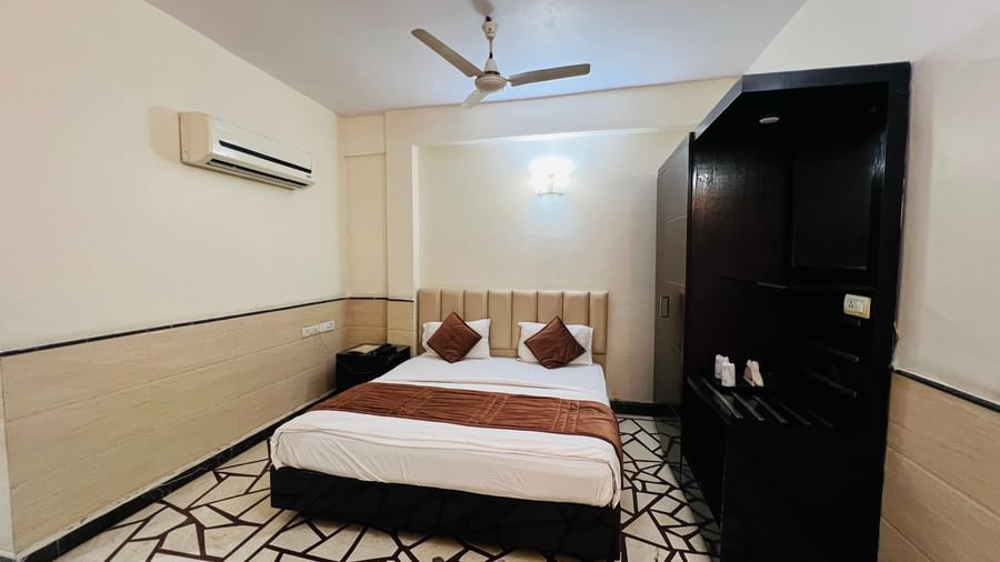 A well-furnished hotel room featuring a comfortable bed with red pillows and dark wood furniture, offering a restful stay. | Suite | Hotel Aadhar