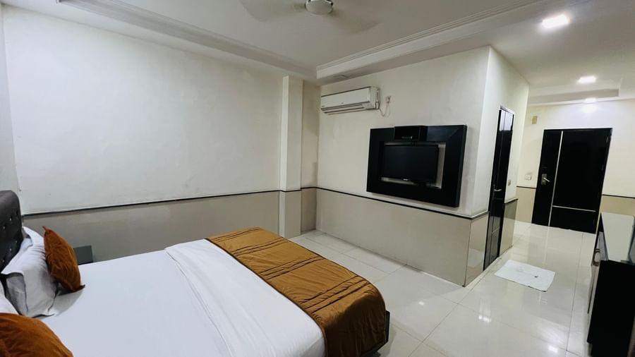 A modern hotel room with a neatly made bed and a flat-screen TV on the wall, creating a comfortable and entertaining space. | Suite | Hotel Aadhar