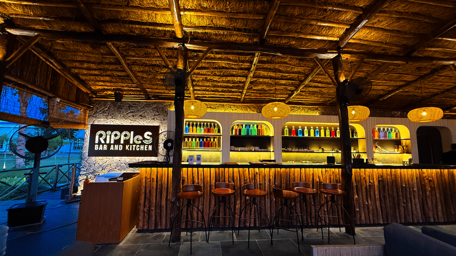 The bar section of Ripples Cafe and Bar at Hotel Sonar Bangla, Kolaghat, showcasing its illuminated logo, well-lit bar shelf, and spacious bar counter with stools.