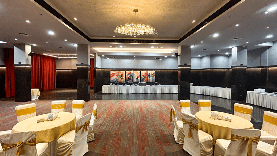 Elegant banquet hall with chandelier, carpet floor, stage, and round tables at Infiniti Hotel, Indore.