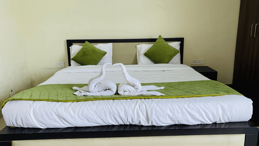 A close-up of a neatly made bed with green cushions and folded towel swans placed at the centre at Livbox Rudrapur.