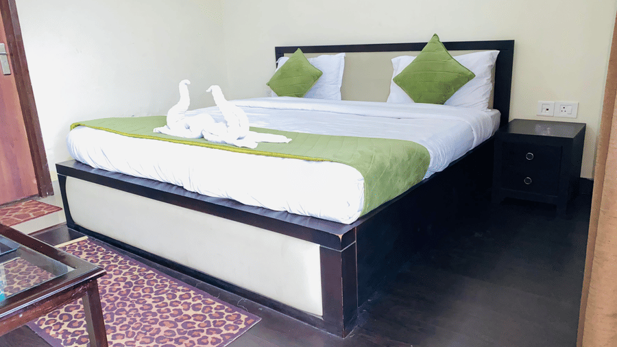 Double bed with green cushions and towel swans in a guest room at Livbox, Rudrapur.