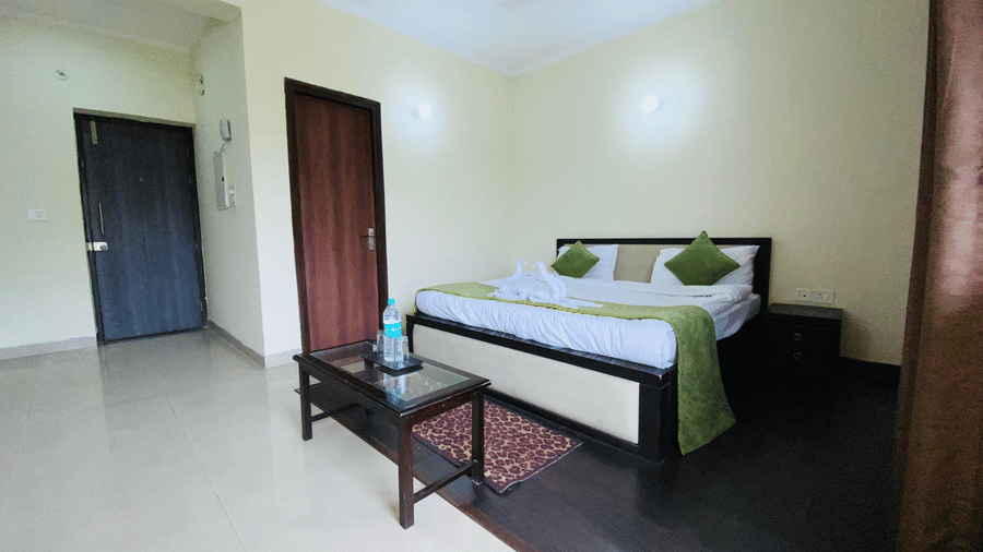 A tidy bedroom with a double bed, green cushions, a glass-topped table, rug, and wooden doors in a spacious setting at Livbox Rudrapur.
