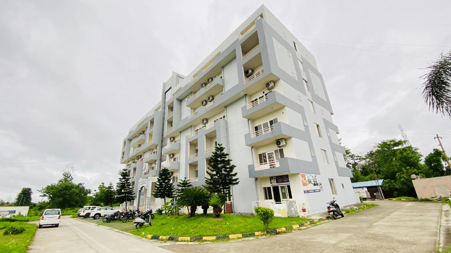 The facade of multi-storey Livbox, Rudrapur featuring the balconies, greenery, and a curved driveway in the foreground.