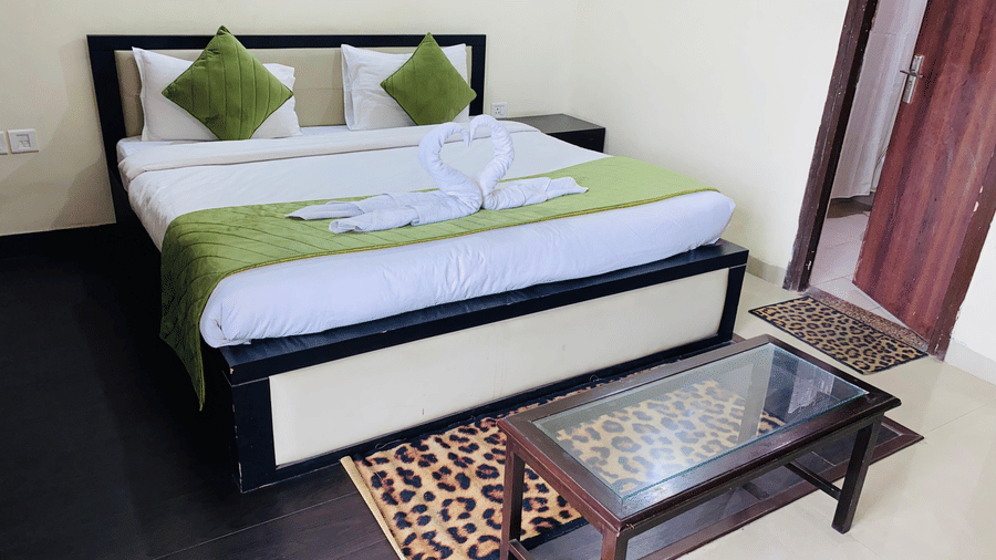 Double bed with green accents, bedside table, printed rug, and a glass-topped table at Livbox, Rudrapur.