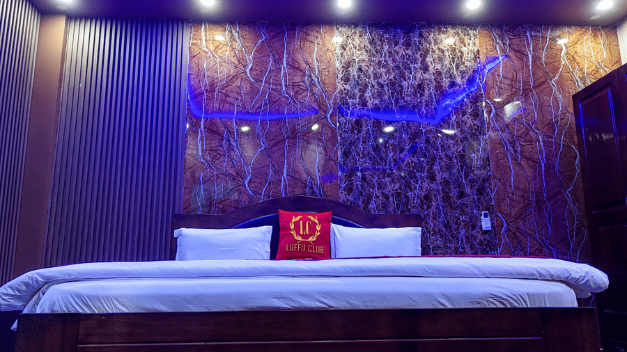 Wide view of a hotel bed against a dark, textured wall with recessed blue lighting - Luffu Club