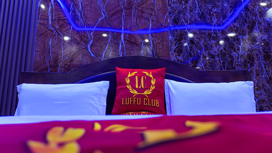 Close-up of a hotel bed with white pillows and a red cushion displaying a 'Luffu Club' logo - Luffu Club
