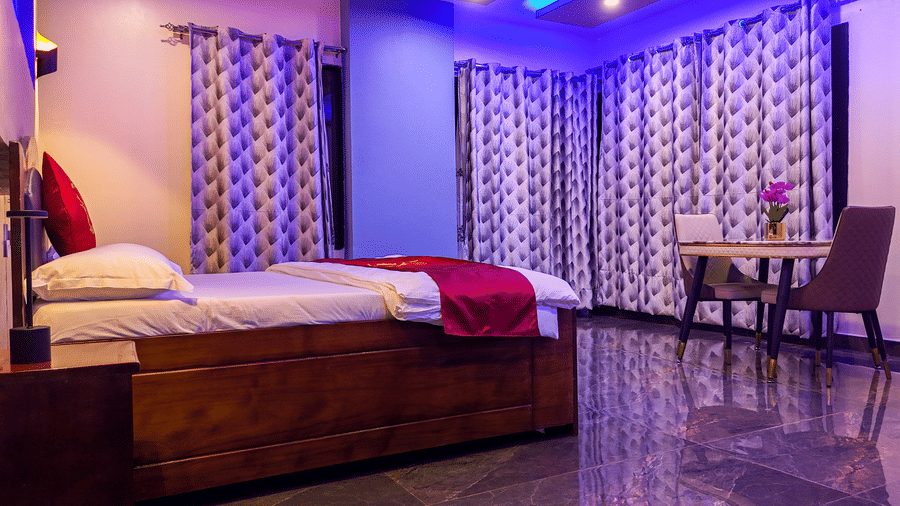 Interior view of a spacious room with a bed, small table and 2 chairs, patterned curtains, and vibrant purple lighting - Luffu Club
