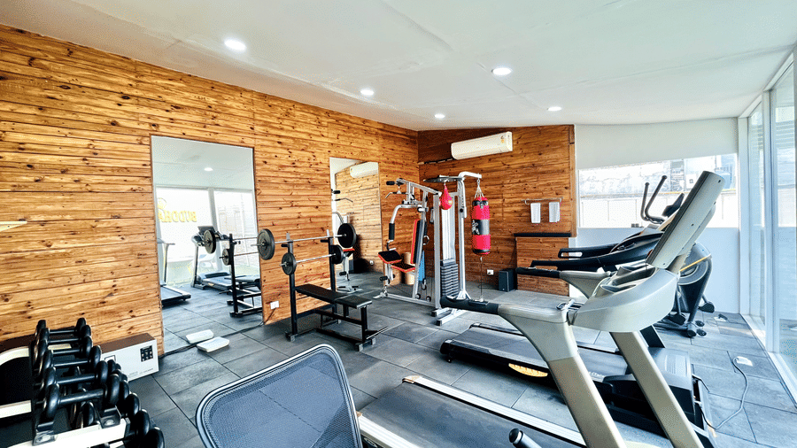 Bright workout facility with multiple treadmills, exercise machines, full-length mirrors, and warm wood accent walls.