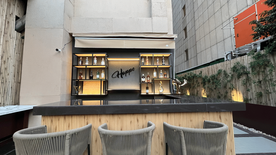 A close-up view of grey woven bar stools arranged along a modern outdoor wooden bar counter.