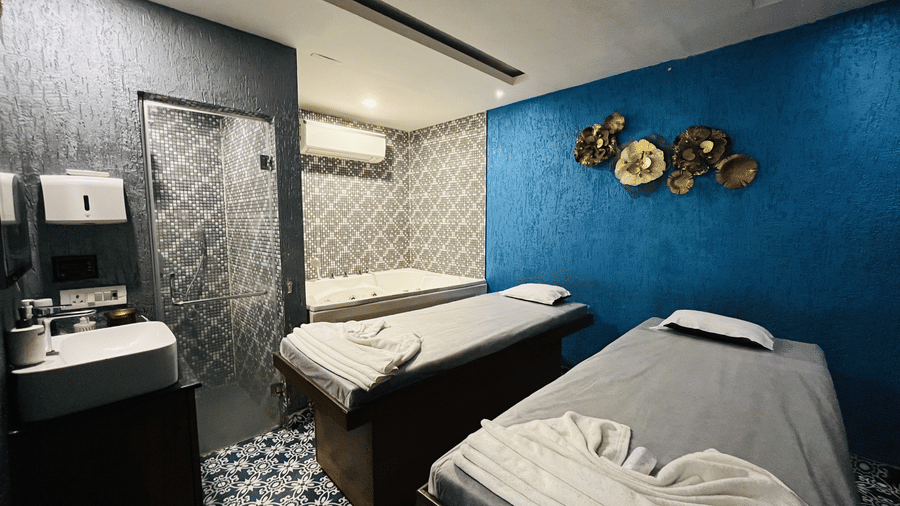 Relaxing wellness spa treatment room with two massage beds and a blue accent wall.