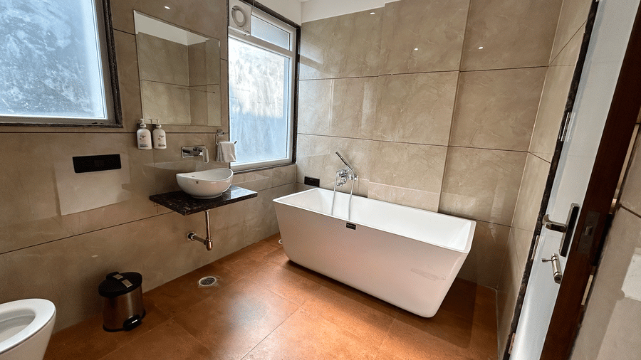 A spacious, modern bathroom featuring a sleek freestanding white bathtub and stone-tiled walls at Pravasa Stay Bapat Square, Indore.