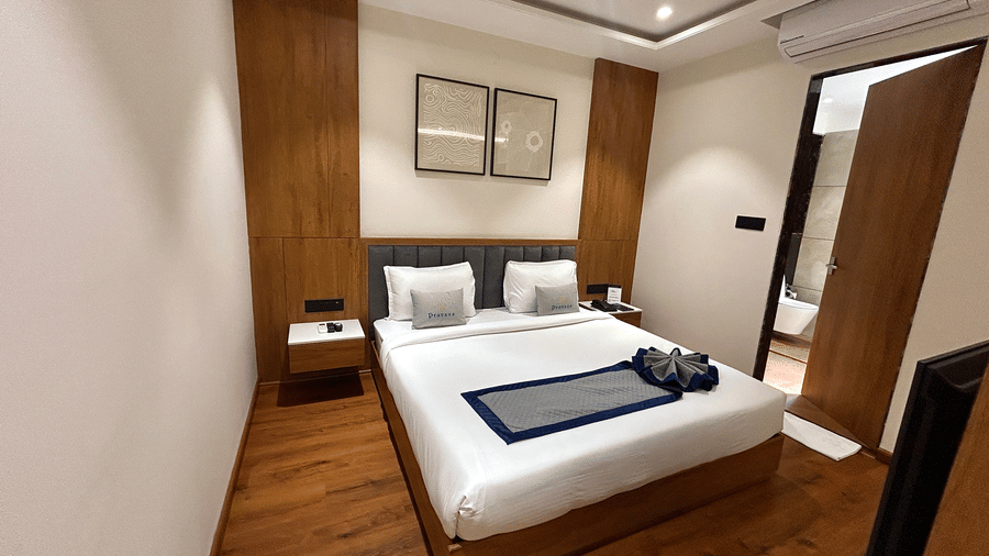 A bright, contemporary hotel bedroom featuring a queen bed with white linens and wooden wall paneling at Pravasa Stay Bapat Square, Indore.