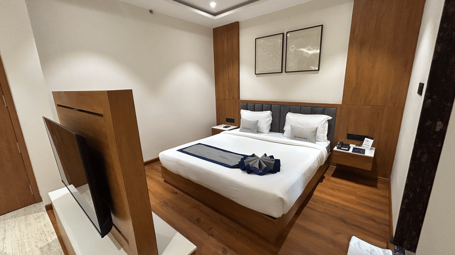 A wide-angle view of a luxury hotel room highlighting the bed, decorative wall art, and elegant wood accents at Pravasa Stay Bapat Square, Indore.