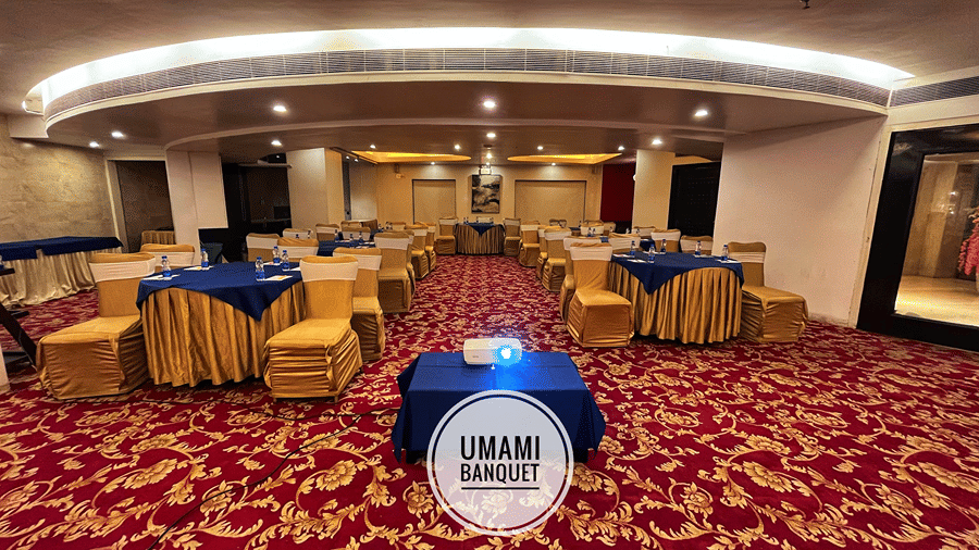 Front view shot of the Ummami Banquet Hall with chairs and tables arranged for a meeting and a projector kept on a small table in the middle - Senses Hotel