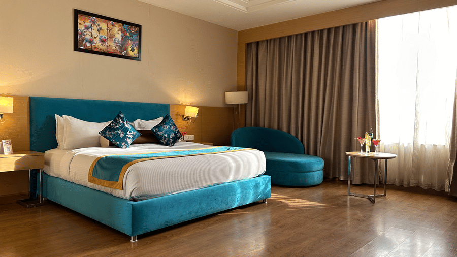 Guest room with king bed, lounge seating area, artwork above bed and window view at The Conway, Meerut