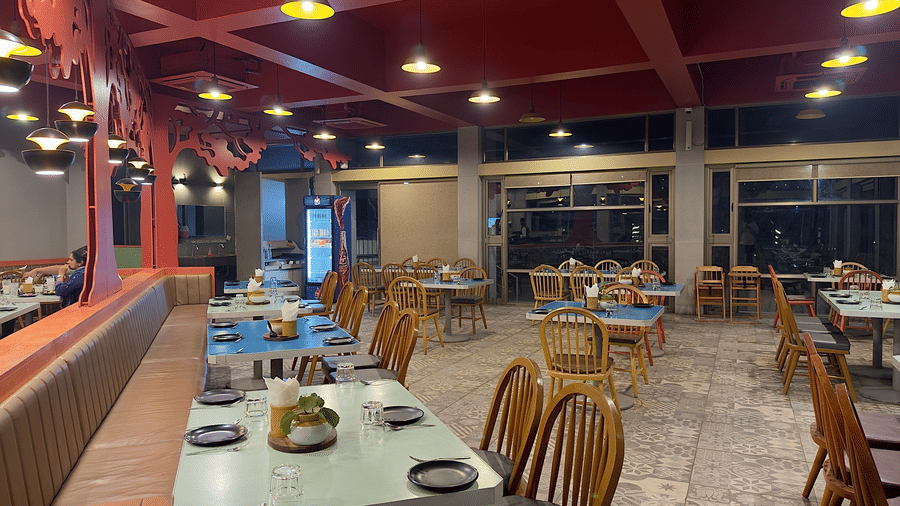 The restaurant at Vinti Resort, Ambaji, warmly lit for dinner, features a striking pink ceiling and comfortable tables set for dining.