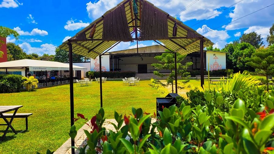 Covered area with tables lined under a beige canopy amidst lush greenery. | Vistar Resort, Bengaluru