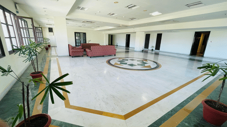 A side view of Raj Vilas Hall featuring potted plants evenly spaced around the tiled floor with sofas at the background.