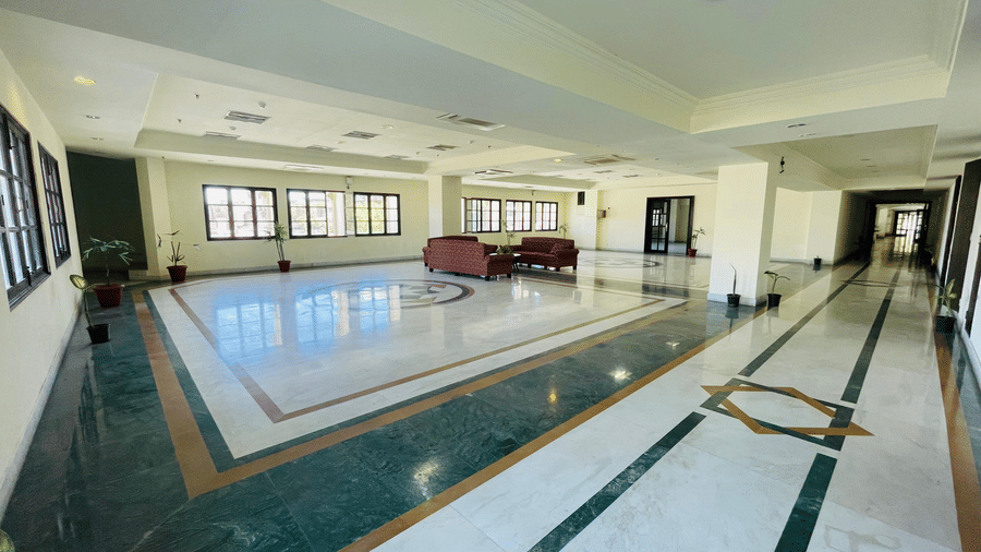 Side wide angle view of Raj Vilas Hall with decorated titled floor, sofas and windows.