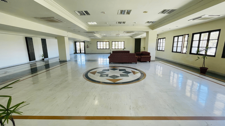 An indoor view of Raj Villas Hall with decorated titled floor, featuring sofas and windows across the room.