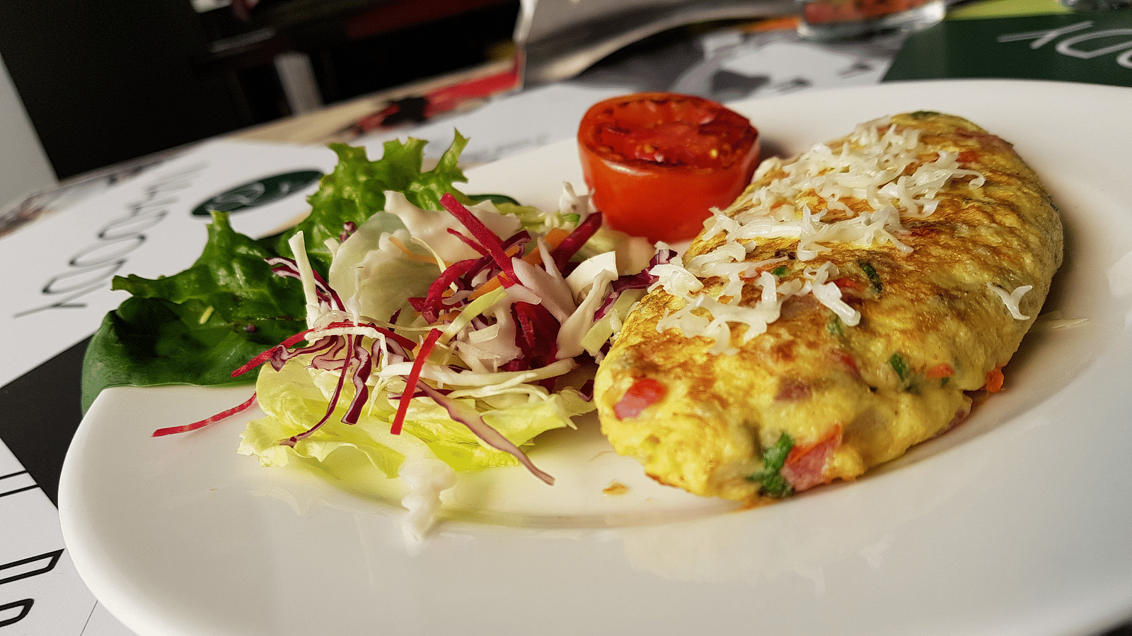 A plate of omelette with a side salad. The omelette is golden brown and filled with vegetables. The salad is green and includes tomatoes and other vegetables.