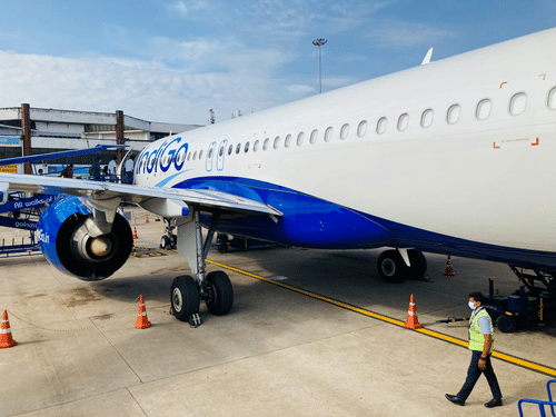 Airplane parked on airport runway with ground staff, cones, and airport equipment visible around the aircraft.