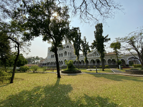 Aga Khan Palace rises beyond a wide green lawn, framed by tall trees.