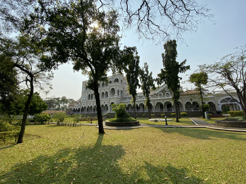Aga Khan Palace rises beyond a wide green lawn, framed by tall trees.