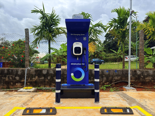 An electric vehicle (EV) charging point stands in an outdoor area surrounded by trees under a cloudy sky at MGM Whispering Wind's