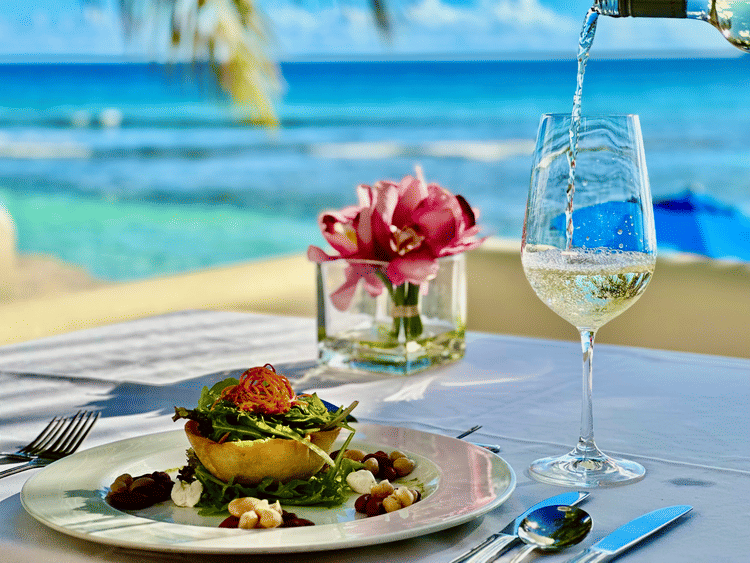 Close-up of an elegantly plated vegetarian meal with wine being poured into a glass on an outdoor table overlooking the ocean at The Soco Hotel.
